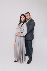 Pregnancy photoshoot of a beautiful couple, future parents in a gray dress and suit