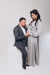 Pregnancy photoshoot of a beautiful couple, future parents in a gray dress and suit
