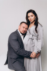 Pregnancy photoshoot of a beautiful couple, future parents in a gray dress and suit