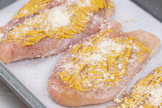 Raw chicken breasts with mustard and cheese ready for baking
