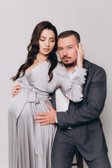 Pregnancy photoshoot of a beautiful couple, future parents in a gray dress and suit