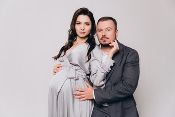 Pregnancy photoshoot of a beautiful couple, future parents in a gray dress and suit