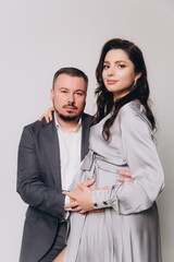 Pregnancy photoshoot of a beautiful couple, future parents in a gray dress and suit
