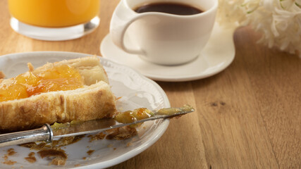 Toasted croissant with orange marmalade spread, fresh orange juice and an espresso coffee for breakfast on a wooden table. Continental breakfast  Close up.