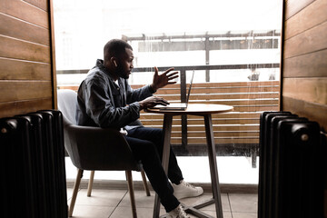 Pensive African American businessman looking at laptop screen, leads video confirmation. With colleagues, he discusses a strategy for an online project, solving problems, working on a complex task.