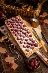 rectangular homemade open short crust pie or tart with white cream and raspberries on wooden white board stands on rustic table, selective focus