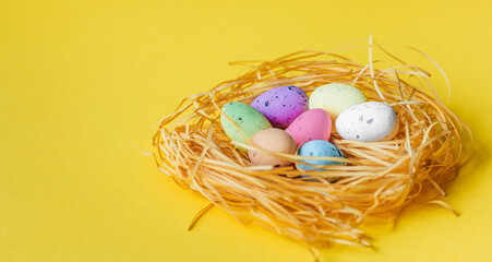 Colorful Easter eggs lie in the nest on a yellow background. The concept of the holiday is Easter, Christ is resurrected. Banner. A place for text.
