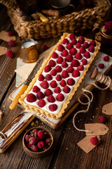 Obraz na płótnie Canvas rectangular homemade open short crust pie or tart with white cream and raspberries on wooden white board stands on rustic table, selective focus