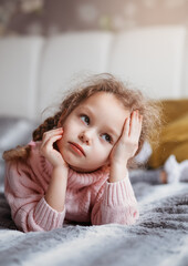 Fototapeta premium Little girl lies on the couch and holds on to her head