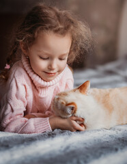 Obraz premium Little girl lies on a bed with a cat