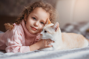 Fototapeta na wymiar Portrait of a little girl and her pet cat lying on the bed