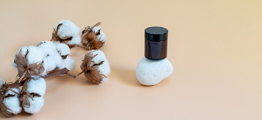 Glass jar with cosmetics and natural cotton branch on the beige background. Mockup banner photo with copy space for displaying your natural eco friendly product.