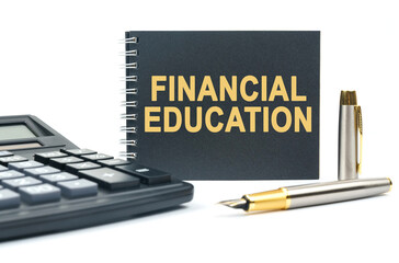 On a white background, there is a calculator, a pen and a black notebook with the inscription - FINANCIAL EDUCATION