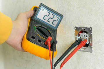 Male electrician checks the voltage of an outlet on a white wall with a multimeter in the house...