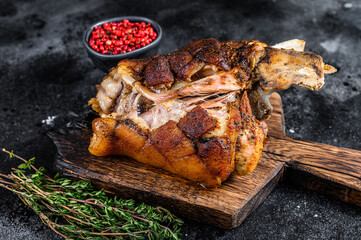 Roasted pork knuckle eisbein on a wooden board with herbs. Black background. Top view - obrazy, fototapety, plakaty