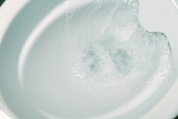 Close-up of flushing water in a white rimless toilet bowl
