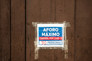 Stock photo of covid19 restrictions sign in wooden door. Translation: "Temporary maximum capacity for Covid-19, 70 people".