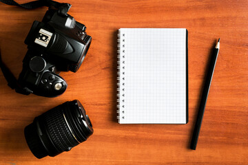 Photo camera and lens with a blank notepad on a wooden table. Photographer's notebook. Photography lessons concept.