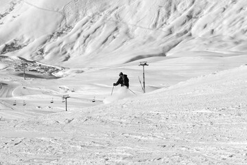 Skier descends on snowy ski slope in sun winter evening