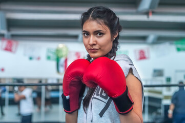 Young attractive latin woman boxer wearing red gloves training on boxing ring.  With a determined...