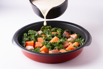 Cooking casserole of salmon, kale, eggs, cream in a black round skillet on a white background.