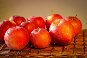 Several ripe red apples stand on a wicker basket illuminated by rays of the sun