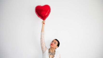 A woman holding a red heart balloon over her head on a white background.