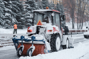 A small red tractor with a brush sweeps snow from the sidewalk near the Kremlin walls during a...
