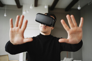 he put a VR helmet on his head. a man in a black jacket is studying a new profession. a programmer plays virtual reality at home.