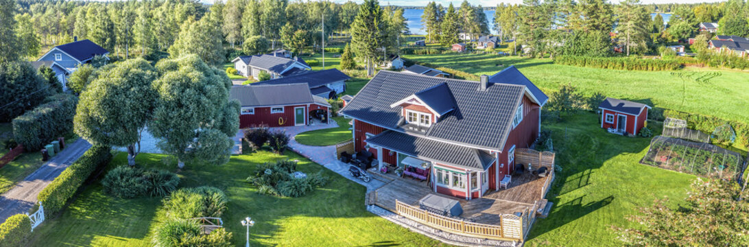 Magnificent aerial panorama photo on traditional Swedish red wooden house - paradise at countryside villa with green lawn, garden. Lake and forest. Warm Sunny Summer evening, Umea, Northern Sweden