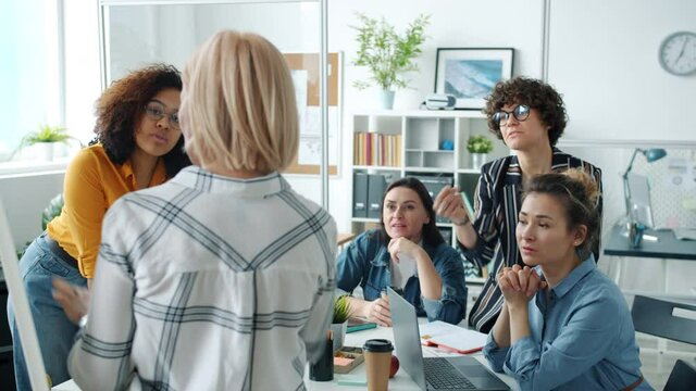Creative team of female employees are talking to mature woman making presentation in glass wall office discussing project. People and teamwork concept.