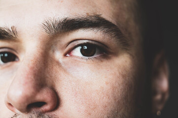 A young man stares at the camera. Brown man's eyes close up. Male face closeup. Lighted male face with small wrinkles and with no bristles.