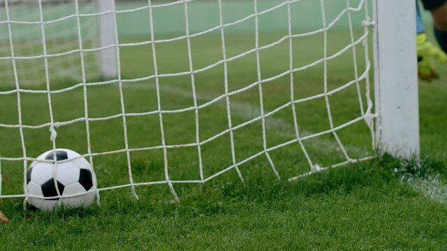 Football soccer game. Detail shot of the ball near the net in the door. A goalkeeper takes it out to resume the play, 4k slow motion