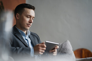 a man in a business suit is sitting in the office. works on a tablet, prints a message in a new messenger. Communicate with partners on a new project, the design of the apartment. Modern style