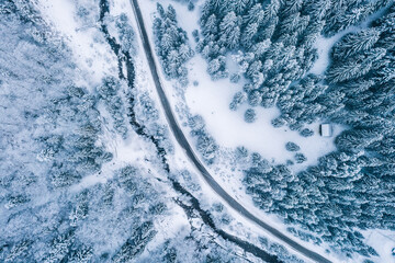 Aerial top view drone shot of the pine and spruce trees forest covered with snow in the Tatra Mountains in Slovakia with a countryside rural road. Transportation and ecology concept image.