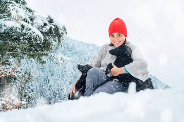 A young woman in warm clothes walking her 2 dogs in snowy mountain outdoor. Female laughing, hugging, and playing with pets. Human and pets winter season concept image