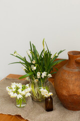 Spring flowers in glass bottles and terracotta vase on rustic wooden table with fabric in room