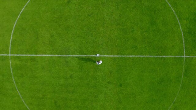 Drone footage of a professional football soccer player at the center point of a football stadium, the shot is moving away from the center. 4k