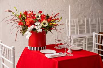 Floral arrangement in red shades of orchids, roses, sunflowers, lilies, alstroemeria and ornithogalum in a red box on a table set for a romantic dinner. Professional work of a florist