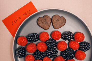 Raspberries with blackberries and biscuits on a plate next to a note that says 