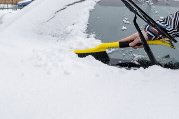 Naklejka premium Man brushing snow and ice from windscreen of car with brush. Person cleaning fresh snow after snowstorm from car in the winter.