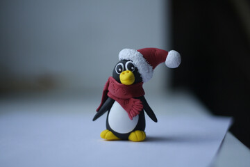 new year penguin in a santa claus  hat with pompon and red scarf sits on a white background and stares intently