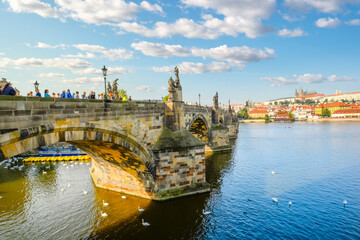 Late afternoon in Prague Czechia as tourists walk across the Charles Bridge of the River Vltava with St Vitus Cathedral and Prague Castle in view.