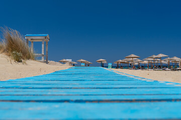 Wooden pathway leading to seashore with blue hammocks and umbrellas on Falasarna beach . Covid-19 lockdown, economy decline concepts.