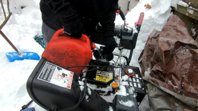 Young Man Filling Up Gasoline In The Snow Blower In The Backyard After The Snow Storm