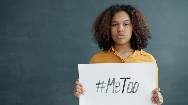 Portrait of African American girl holding MeToo hashtag poster supporting sexual abuse victims standing against grey background. People and social problems concept.