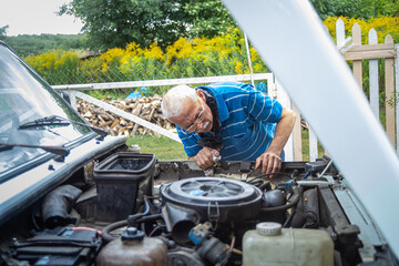elderly man repairs car. Repair engine of old car in yard of house.