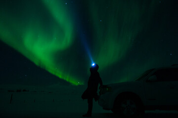 Man standing watching aurora borealis, northern lights witch head torch in North Iceland, Europe