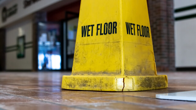A dirty yellow four-sided wet floor sign on a dusty tile ground in London Ontario Canada, February 2021. 