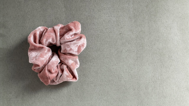 A pale pastel pink velvet hair scrunchie on a light green suede background, well-lit, with room for text or copy, February 2021, Ontario, Canada.
